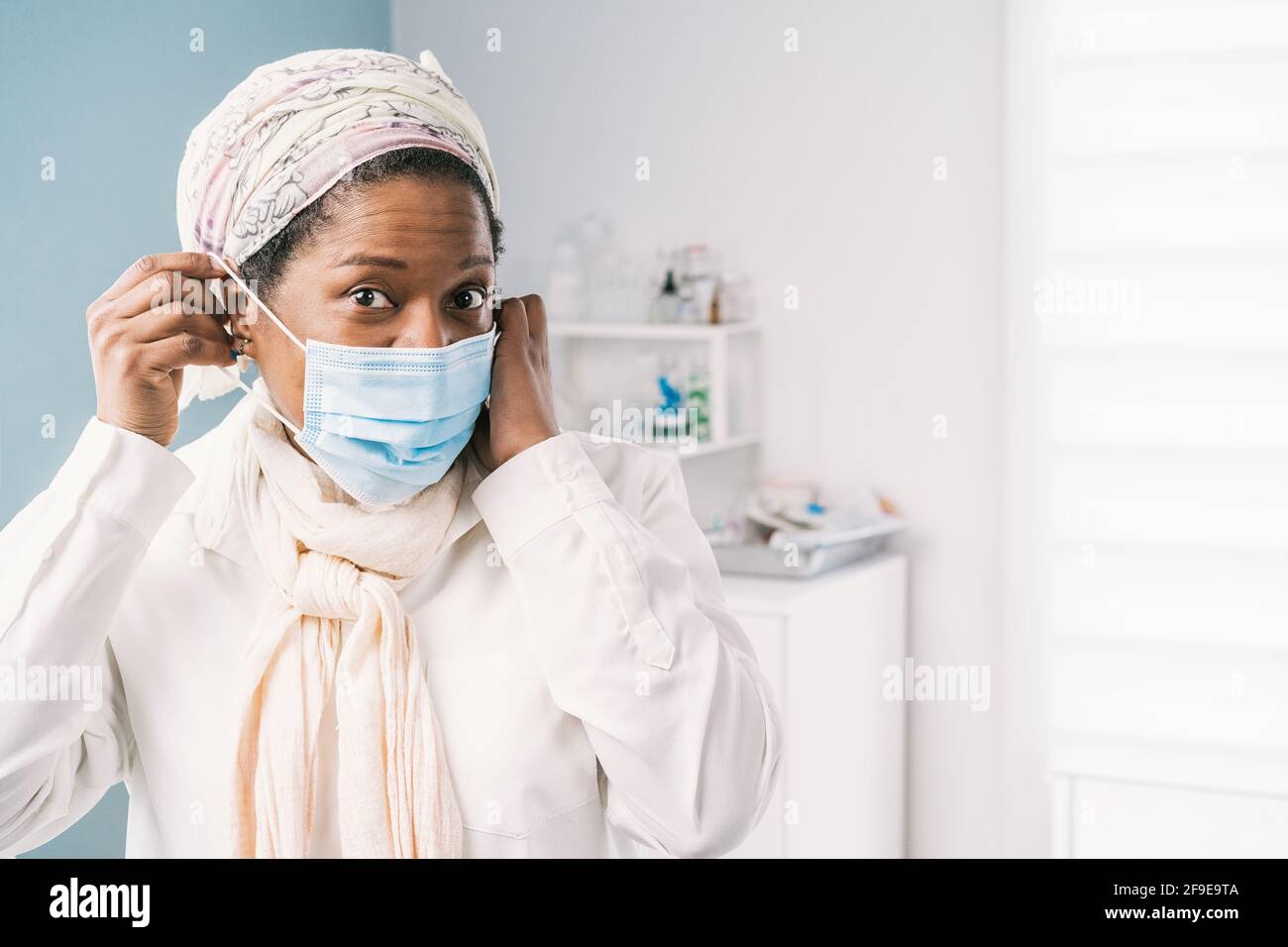 Femme afro-américaine mature avec masque facial assise au lit de la clinique en attente d'un rendez-vous pendant l'épidémie de coronavirus Banque D'Images