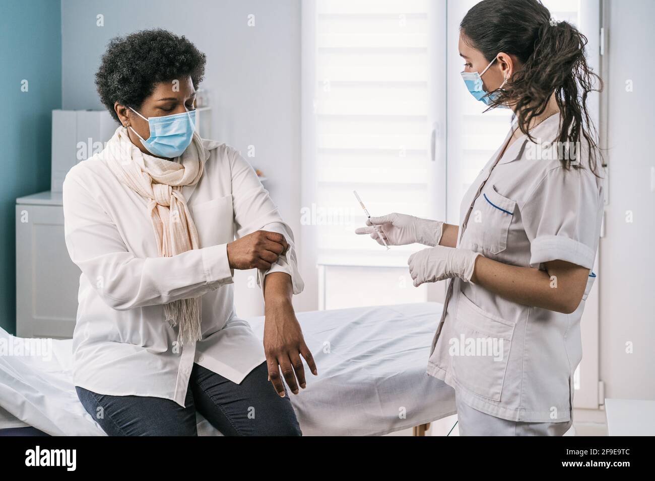 Femme médecin spécialiste en uniforme de protection, gants en latex et masque facial vaccinant la patiente africaine américaine mature en clinique pendant le coronav Banque D'Images
