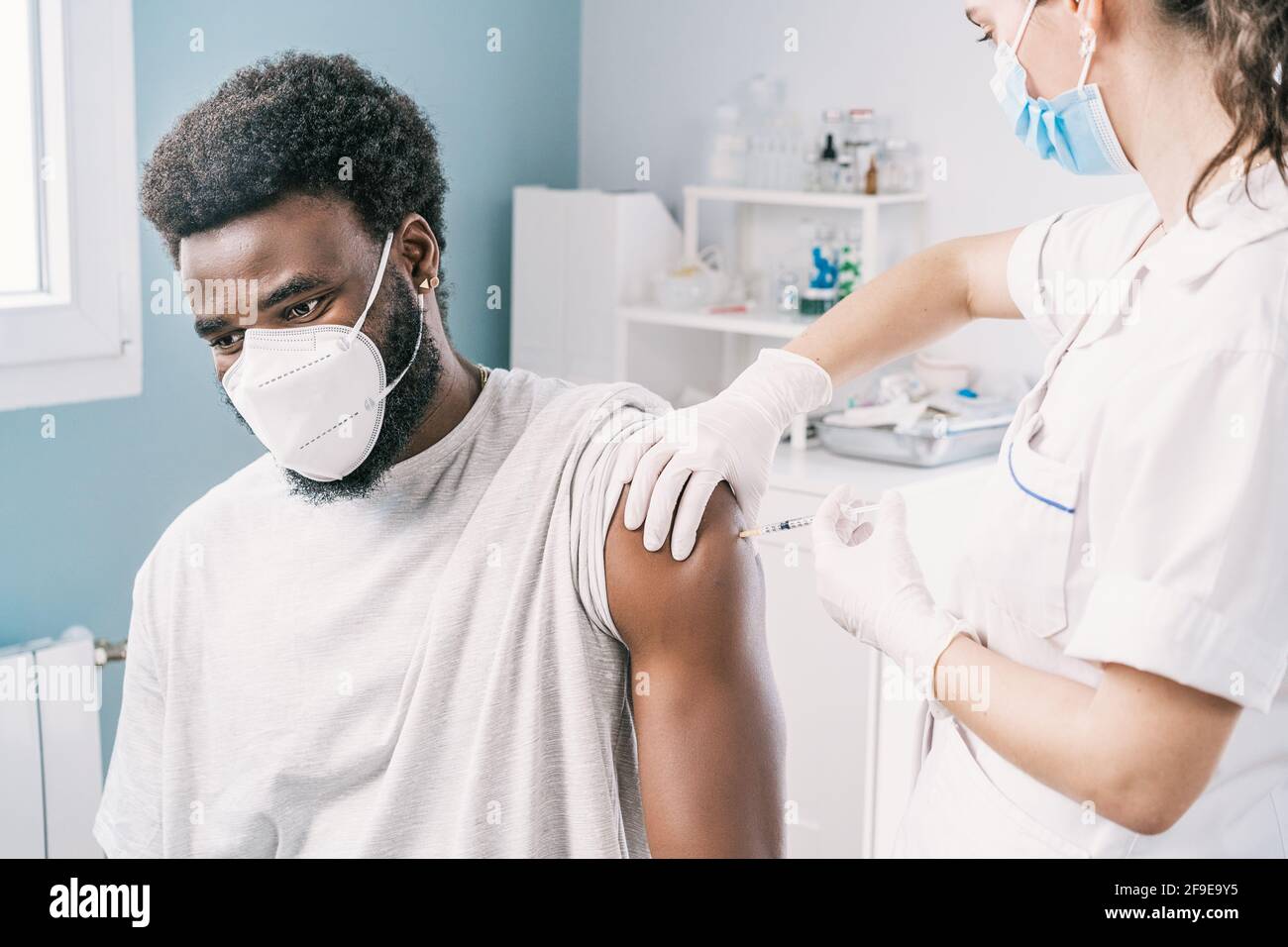 Femme médecin spécialiste en uniforme de protection, gants en latex et masque facial vaccinant l'homme afro-américain en clinique pendant l'outb du coronavirus Banque D'Images