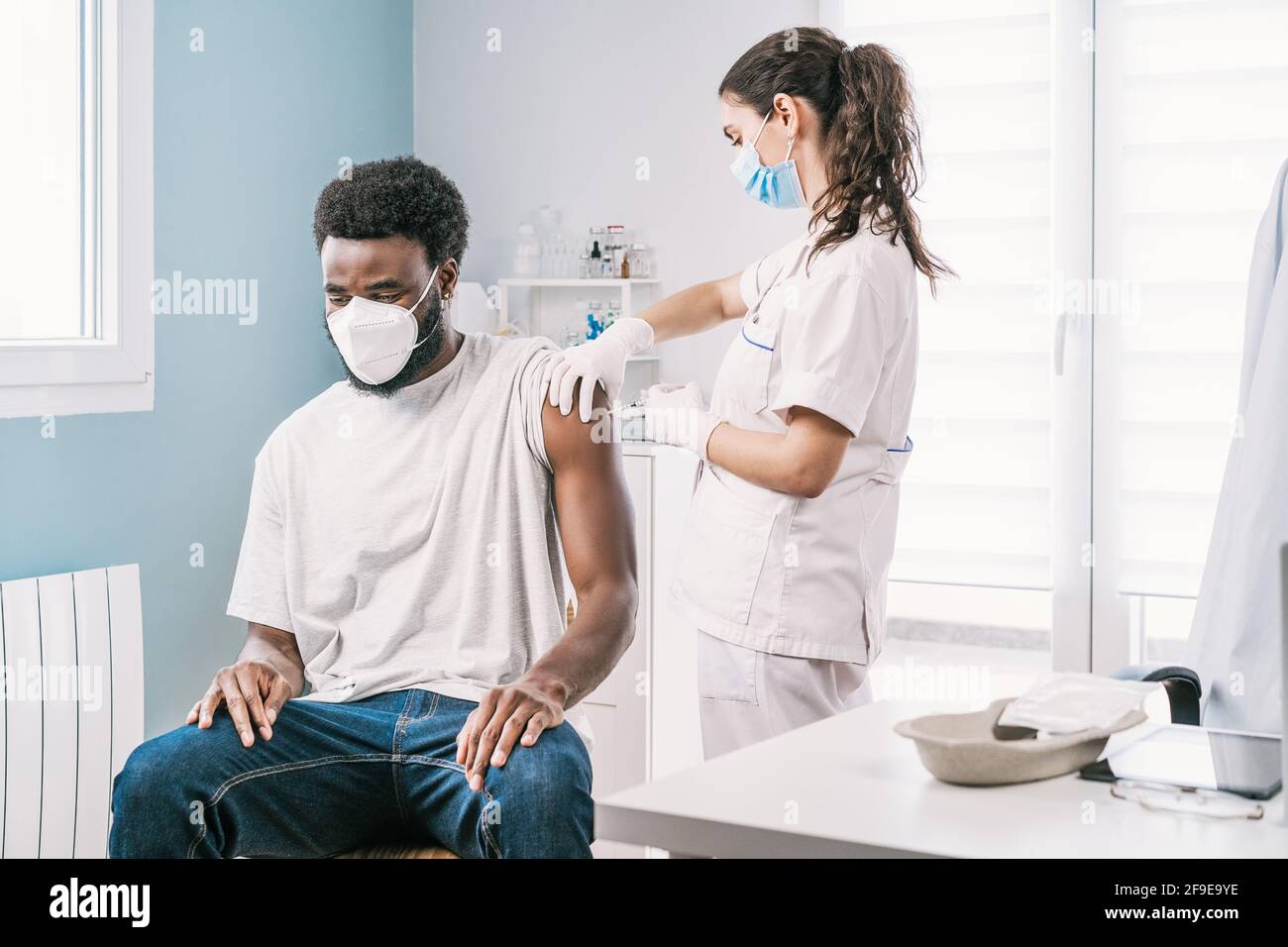 Femme médecin spécialiste en uniforme de protection, gants en latex et masque facial vaccinant l'homme afro-américain en clinique pendant l'outb du coronavirus Banque D'Images