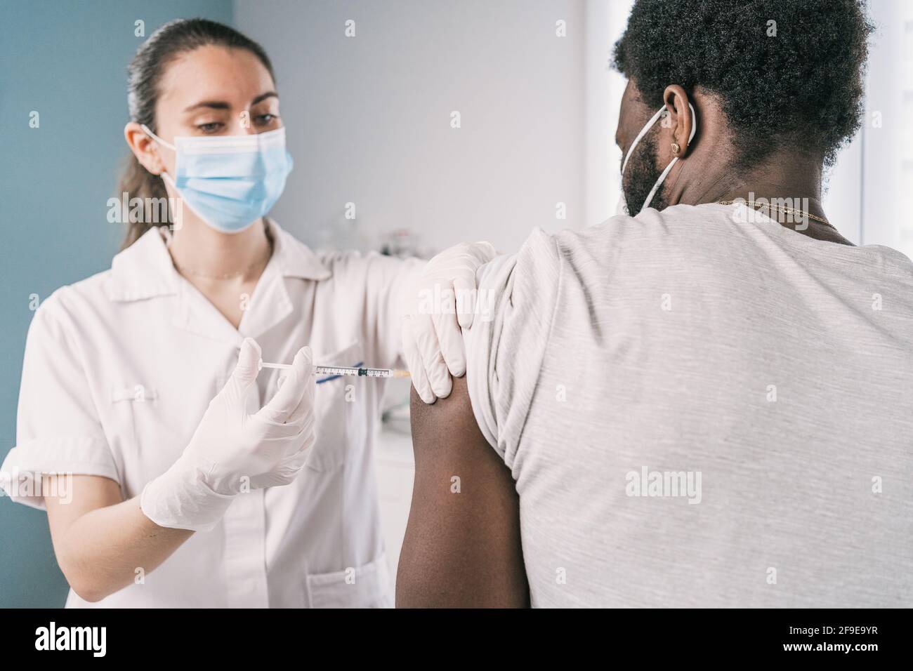 Femme médecin spécialiste en uniforme de protection, gants en latex et masque facial vaccinant l'homme afro-américain en clinique pendant l'outb du coronavirus Banque D'Images