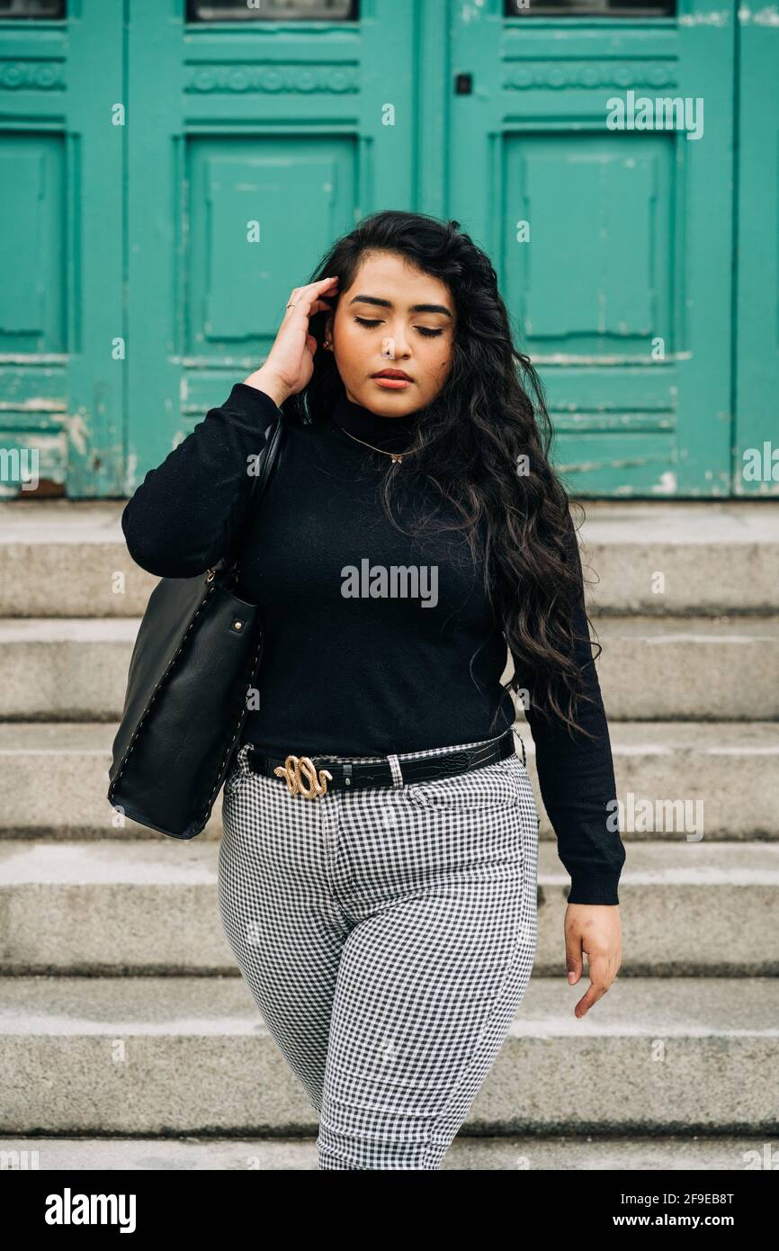 Charmante femme curvy dans une tenue tendance qui se promette dans la rue  de la ville et en touchant les cheveux longs et ondulés Photo Stock - Alamy