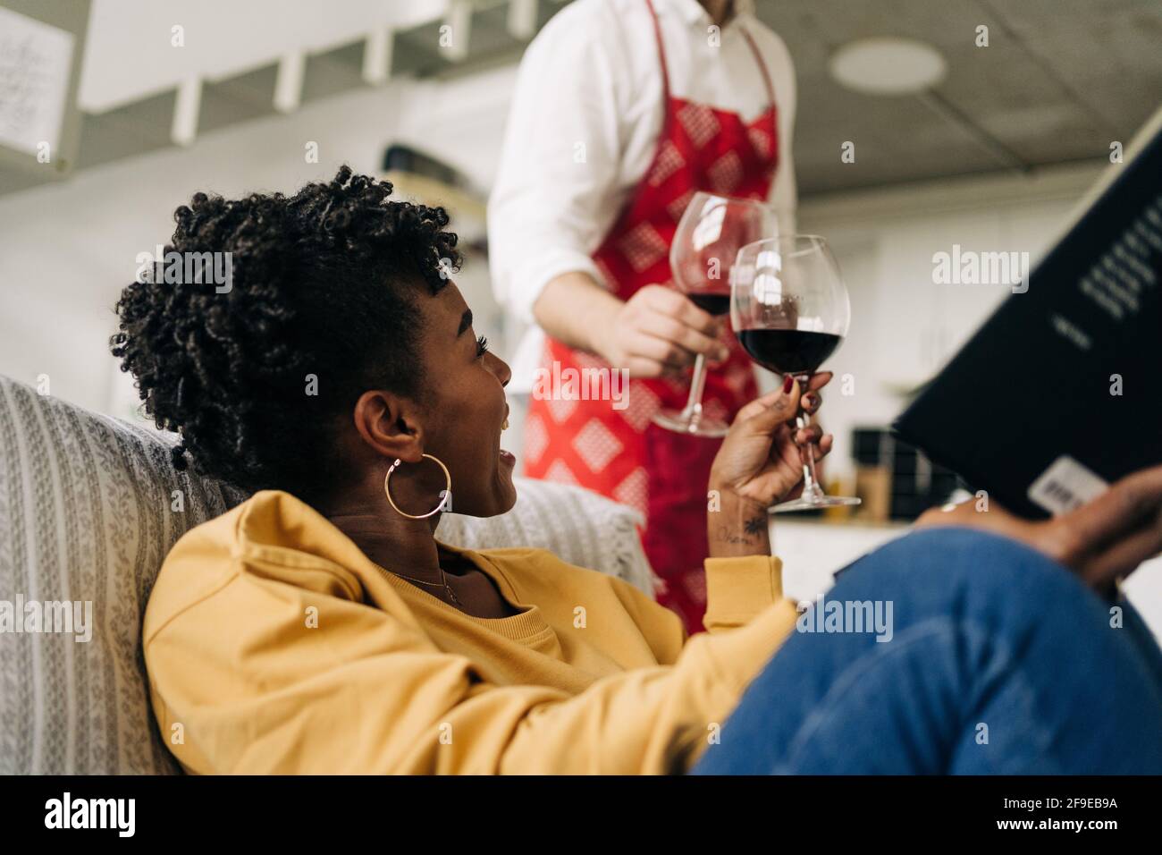 Lunettes à petit angle pour couple multiracial avec vin rouge tout en appréciant le week-end à la maison Banque D'Images