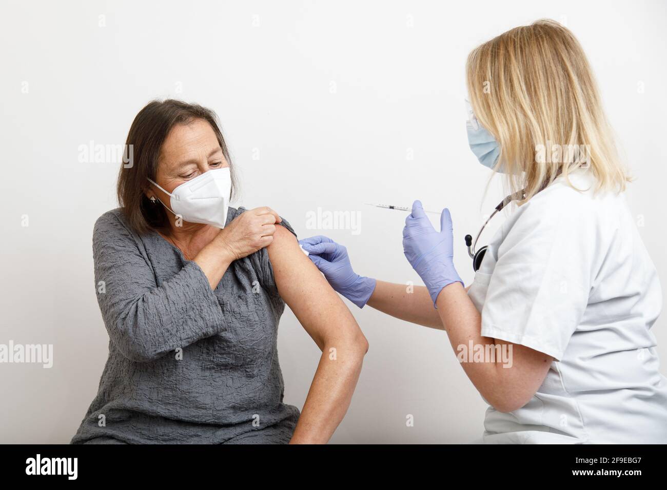Femme médecin spécialiste en uniforme de protection et gants en latex vaccinant patiente sénior en clinique pendant l'éclosion du coronavirus Banque D'Images