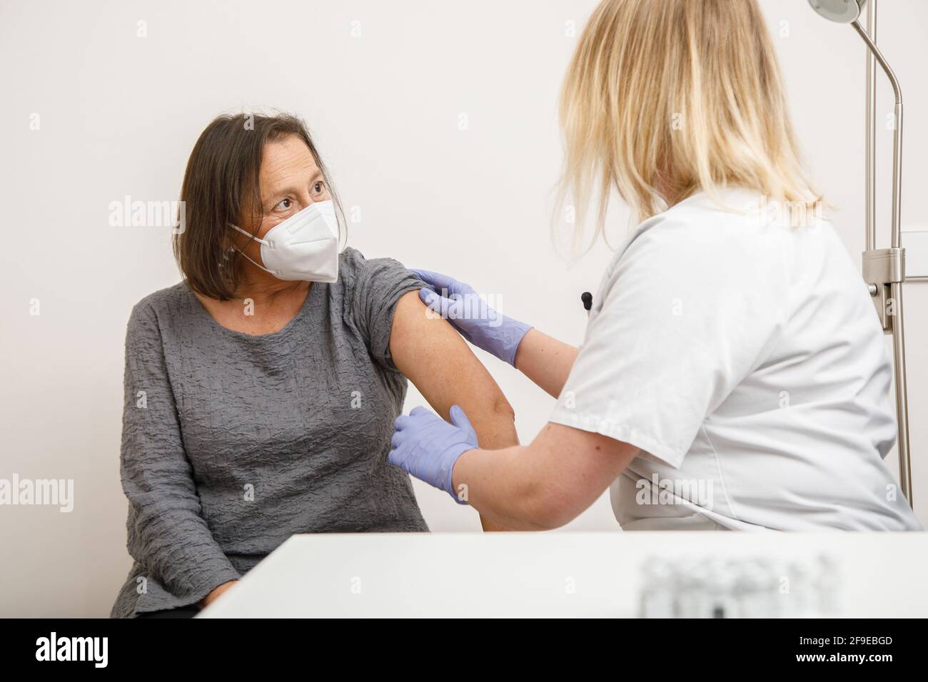 Femme médecin spécialiste en uniforme de protection et gants en latex vaccinant patiente sénior en clinique pendant l'éclosion du coronavirus Banque D'Images