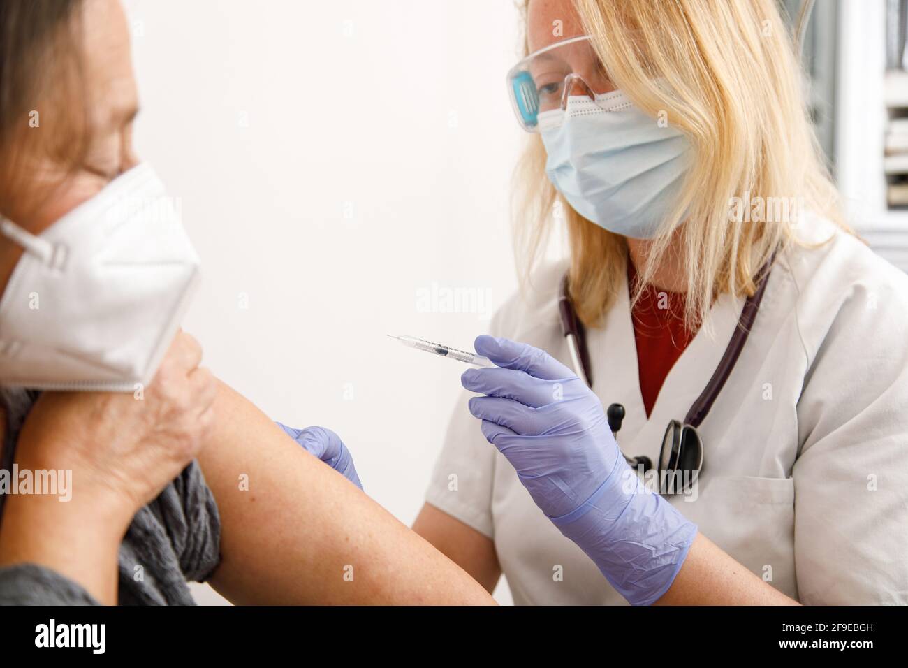 Spécialiste médical de la culture féminine en uniforme de protection et gants en latex la vaccination des femmes âgées en clinique pendant l'éclosion du coronavirus Banque D'Images