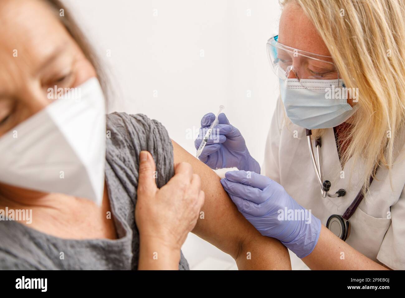 Femme médecin spécialiste en uniforme de protection et gants en latex vaccinant patiente sénior en clinique pendant l'éclosion du coronavirus Banque D'Images