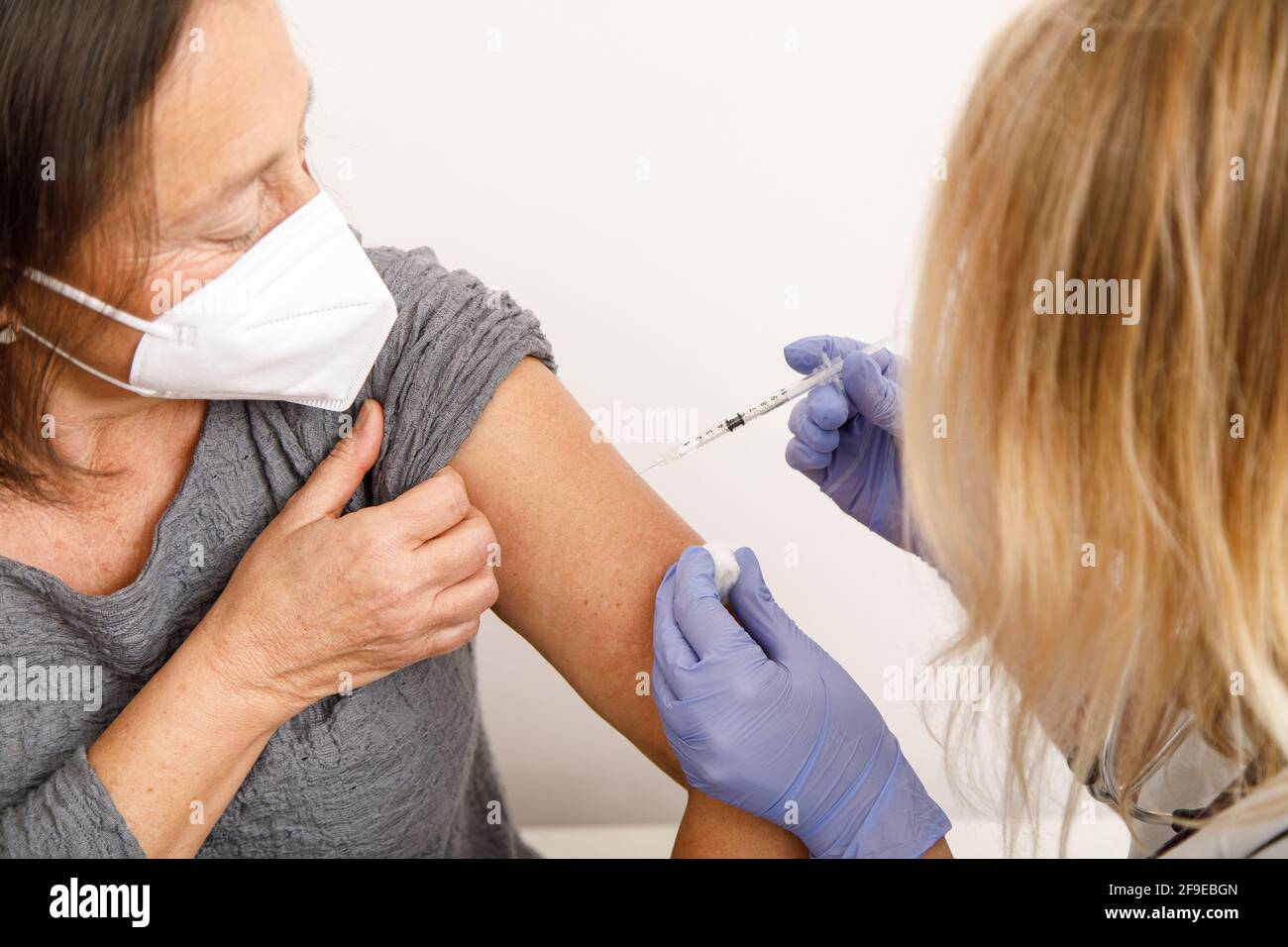 Spécialiste médical de la culture féminine en uniforme de protection et gants en latex la vaccination des femmes âgées en clinique pendant l'éclosion du coronavirus Banque D'Images