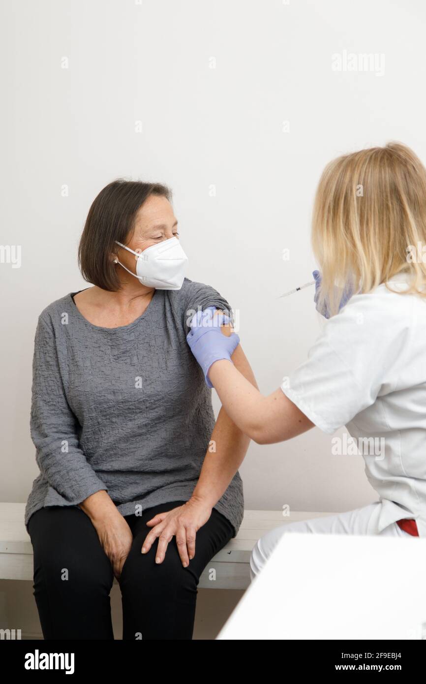 Femme médecin spécialiste en uniforme de protection et gants en latex vaccinant patiente sénior en clinique pendant l'éclosion du coronavirus Banque D'Images