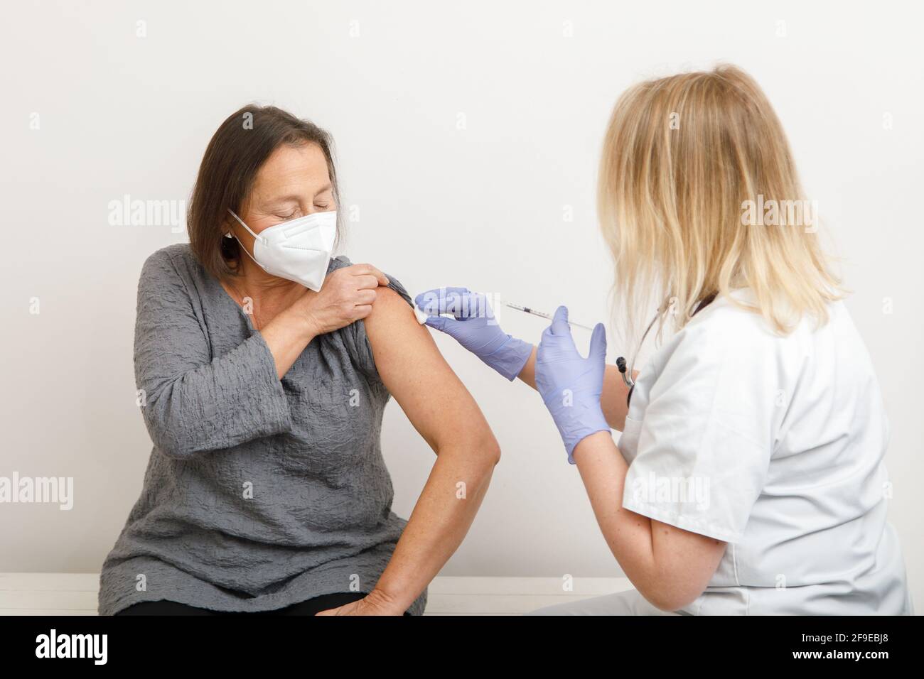 Femme médecin spécialiste en uniforme de protection et gants en latex vaccinant patiente sénior en clinique pendant l'éclosion du coronavirus Banque D'Images