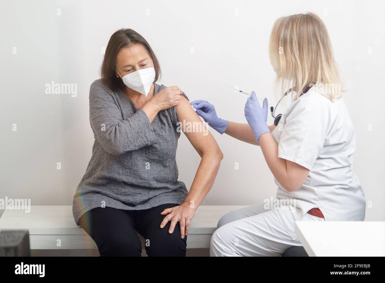 Femme médecin spécialiste en uniforme de protection et gants en latex vaccinant patiente sénior en clinique pendant l'éclosion du coronavirus Banque D'Images