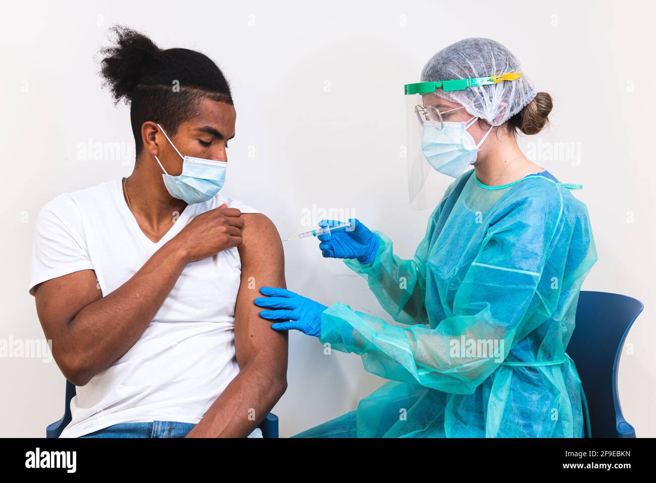 Femme médecin spécialiste en uniforme de protection, gants en latex et masque facial vaccinant l'homme afro-américain en clinique pendant l'outb du coronavirus Banque D'Images