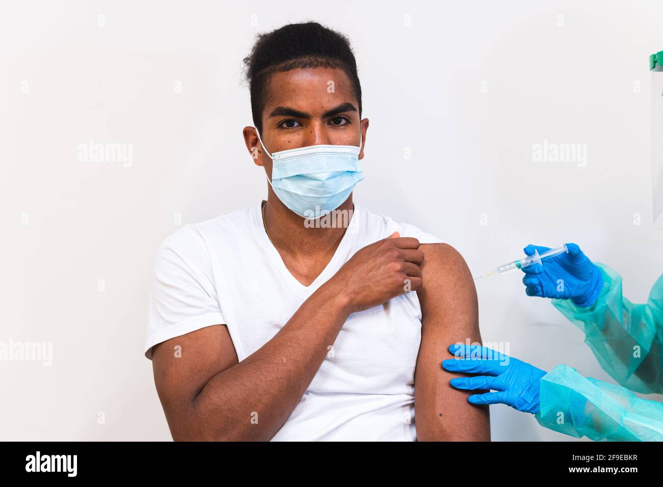 Spécialiste médical féminin en uniforme de protection, gants en latex et masque facial, non reconnaissable, en culture, qui vaccine un homme afro-américain en clinique Banque D'Images