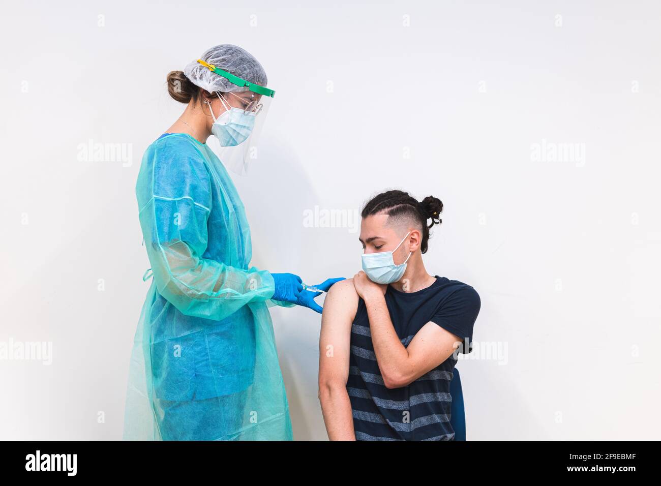Spécialiste médical féminin en uniforme de protection, gants en latex et masque facial vaccinant un patient hispanique en clinique pendant une épidémie de coronavirus Banque D'Images