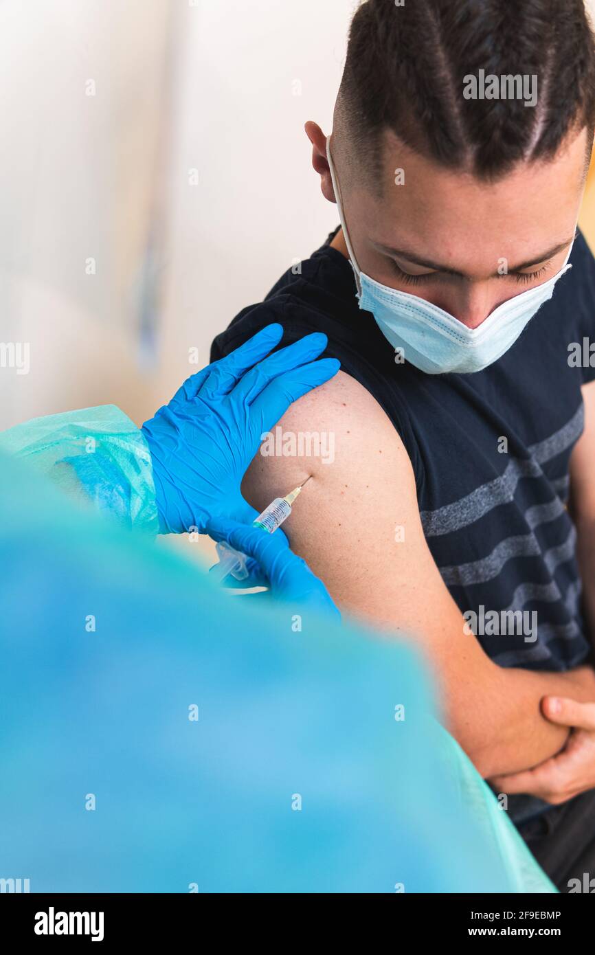 Spécialiste médical de la culture féminine en uniforme de protection, gants en latex et masque facial vaccinant un patient hispanique en clinique pendant l'outbrea du coronavirus Banque D'Images
