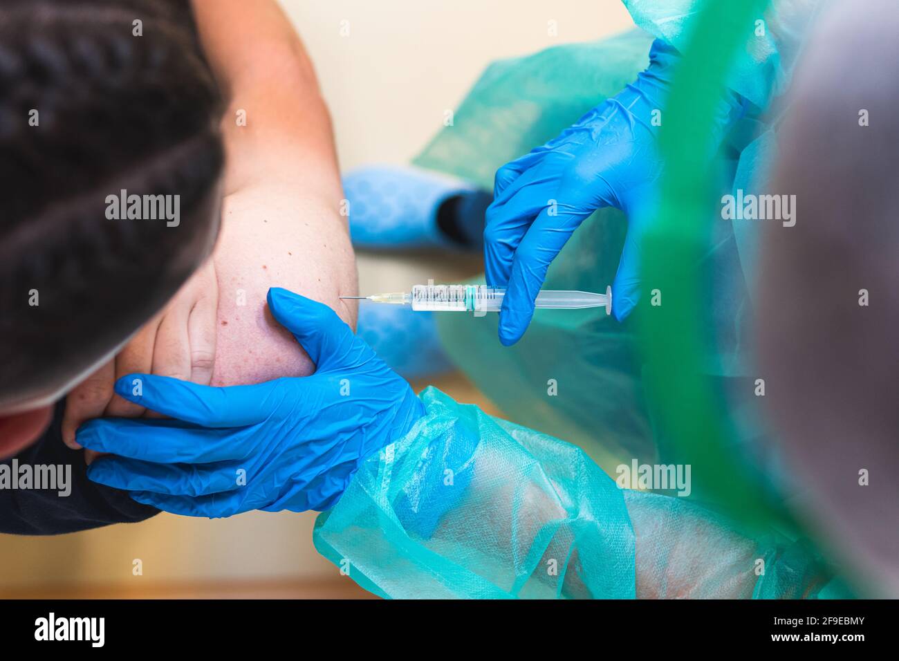 Spécialiste médical de la culture féminine en uniforme de protection, gants en latex et masque facial vaccinant un patient hispanique en clinique pendant l'outbrea du coronavirus Banque D'Images