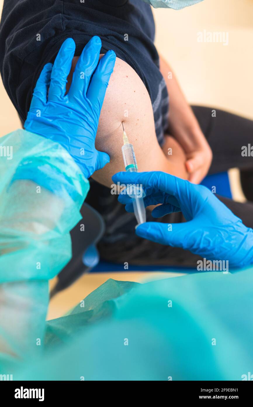 Spécialiste médical de la culture féminine en uniforme de protection, gants en latex et masque facial vaccinant un patient hispanique en clinique pendant l'outbrea du coronavirus Banque D'Images