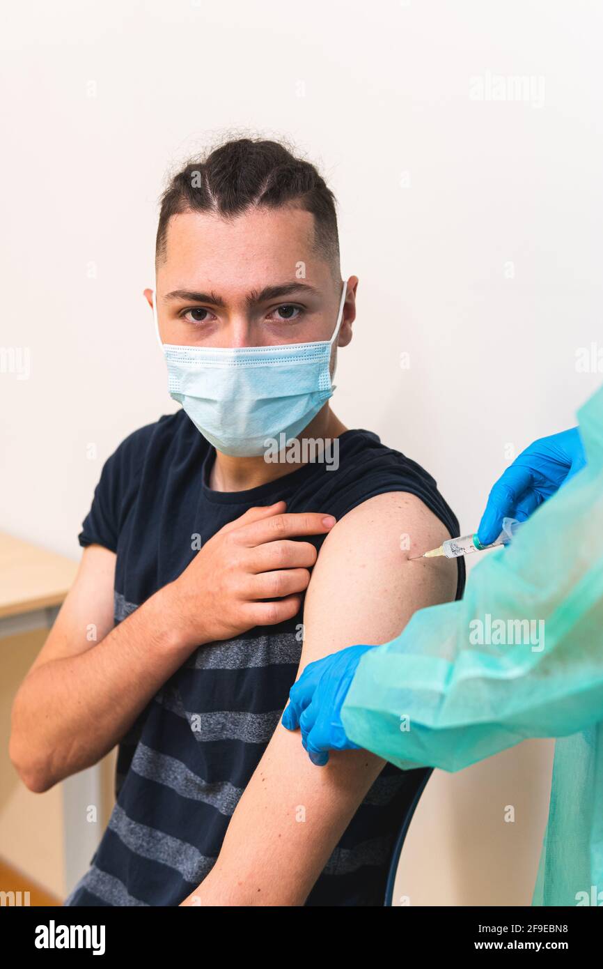 Spécialiste médical de la culture féminine en uniforme de protection, gants en latex et masque facial vaccinant un patient hispanique en clinique pendant l'outbrea du coronavirus Banque D'Images