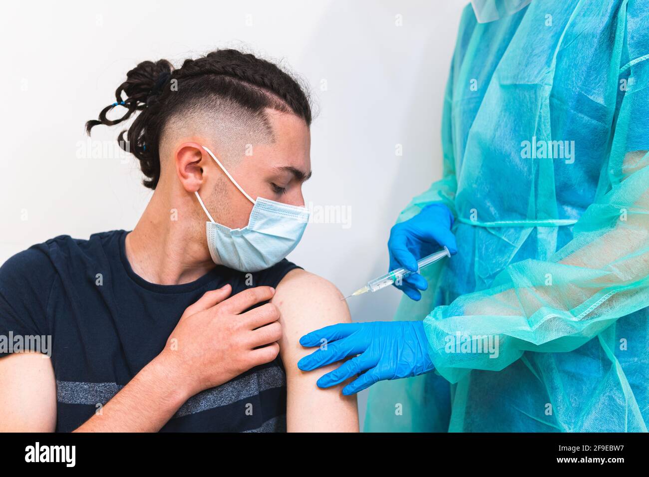 Spécialiste médical de la culture féminine en uniforme de protection, gants en latex et masque facial vaccinant un patient hispanique en clinique pendant l'outbrea du coronavirus Banque D'Images