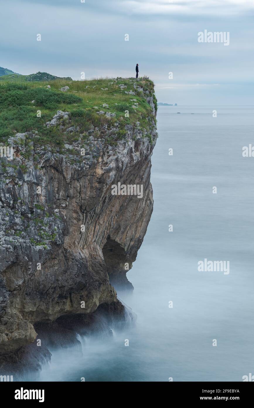 Silhouette de la personne se tenant sur le bord de la falaise rocheuse à proximité mer sur la côte de Ribadesella le jour nuageux dans les Asturies Banque D'Images