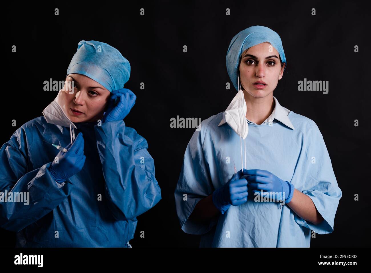 Jeunes femmes collègues en uniformes médicaux qui prennent des masques faciaux en se tenant sur fond noir en clinique Banque D'Images