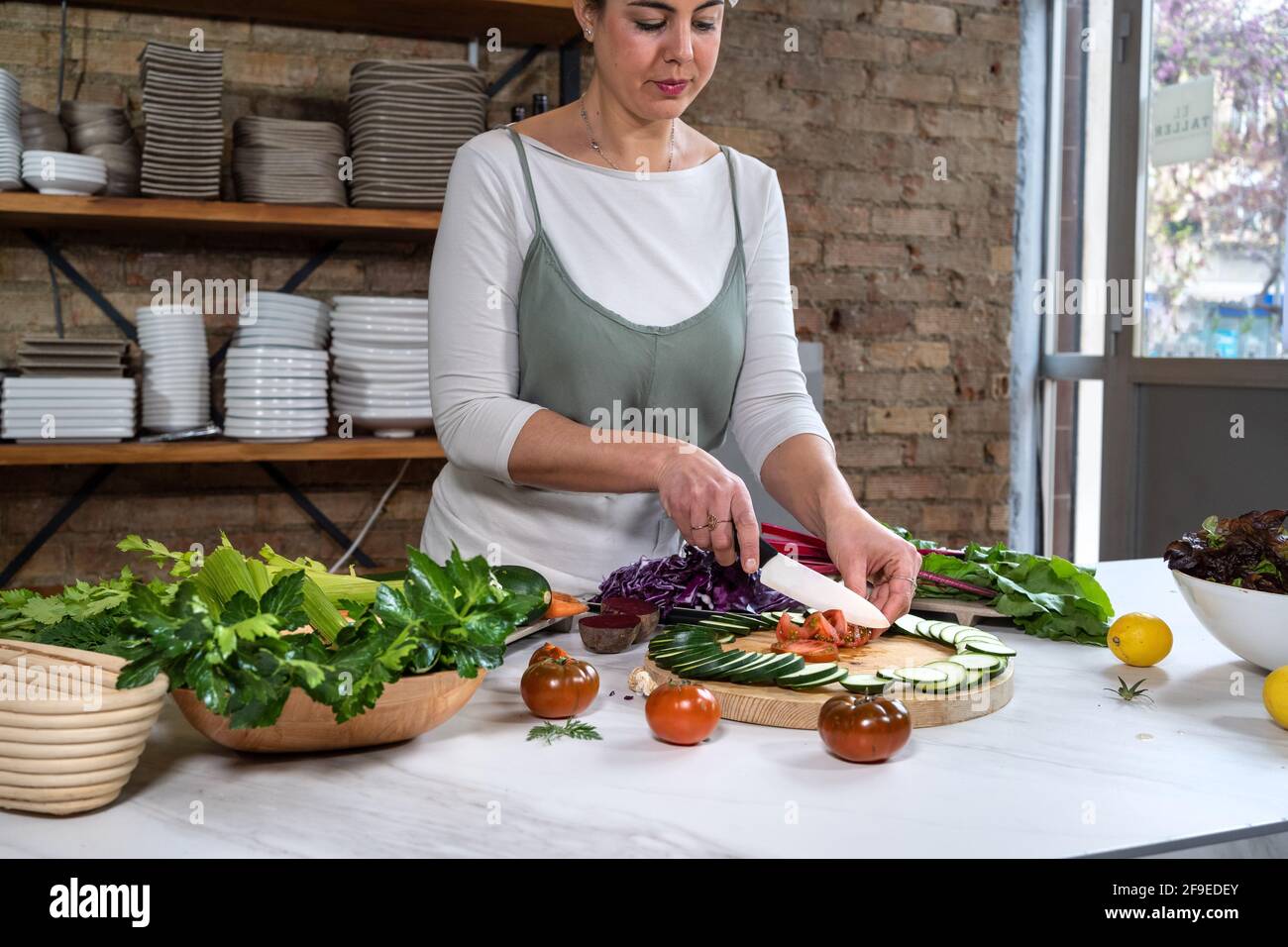 Focus femelle coupant des tomates fraîches mûres parmi les tranches de courgettes pendant processus de cuisson en interne Banque D'Images