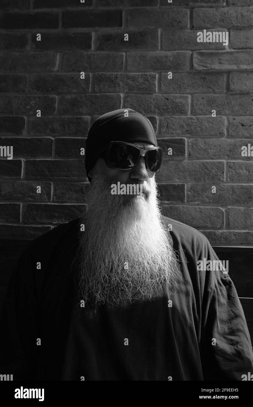 Portrait noir et blanc de l'homme mûr avec un long gris penser à la barbe et porter des lunettes de soleil et un bonnet Banque D'Images