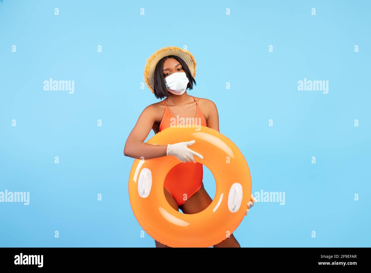 Vacances d'été pendant le verrouillage de covid. Femme noire en maillot de bain, masque facial et gants en caoutchouc tenant l'anneau gonflable Banque D'Images