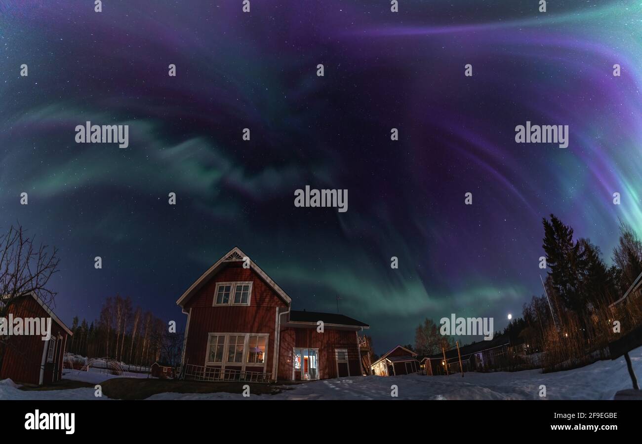 Panorama des aurores boréales dans un ciel étoilé clair, au-dessus de la maison rouge en bois suédois, dans un paysage de campagne. Vert et bleu Aurora Borealis s Banque D'Images