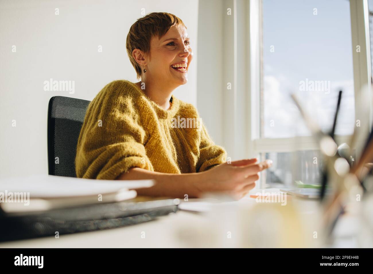 Une femme heureuse assise exécutive au bureau. Femme joyeuse assise au bureau et vue loin dans le bureau. Banque D'Images