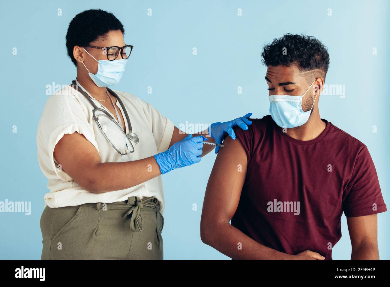 Femme médecin portant un masque facial et des gants donnant le vaccin à un homme sur fond bleu. Homme vacciné par une femme médecin. Banque D'Images
