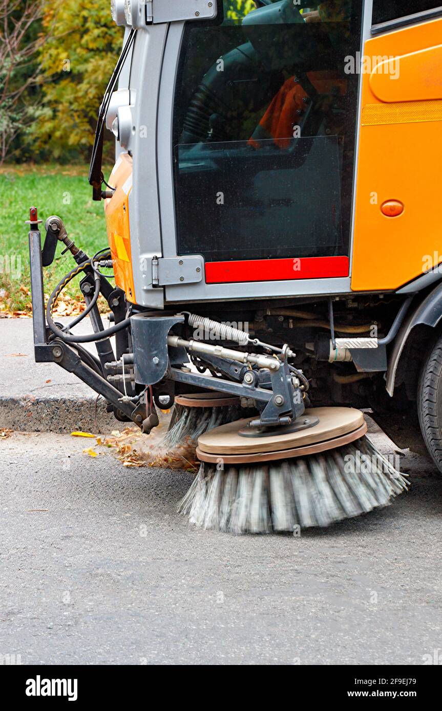 Les brosses rotatives avant du balai ramassent les débris et les résidus de feuilles sur le bord de la route. Image verticale, espace de copie. Banque D'Images