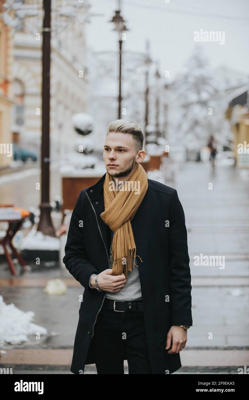 Un jeune homme plein d'assurance dans une tenue d'hiver noire avec un foulard  marron qui se balade dans la ville Photo Stock - Alamy
