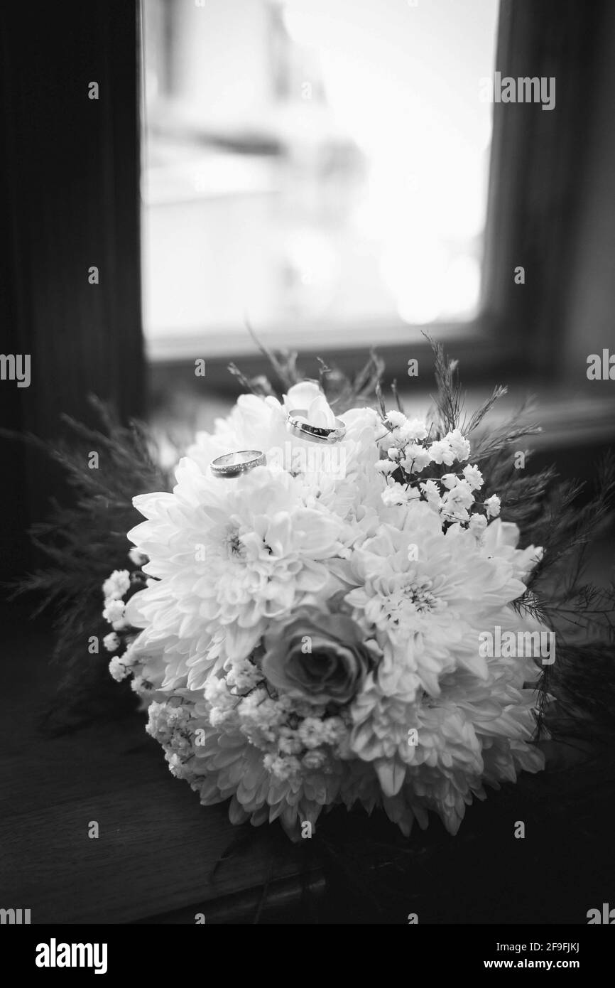 Une photo verticale des anneaux de mariage sur le dessus d'un bouquet de fleurs en niveaux de gris Banque D'Images