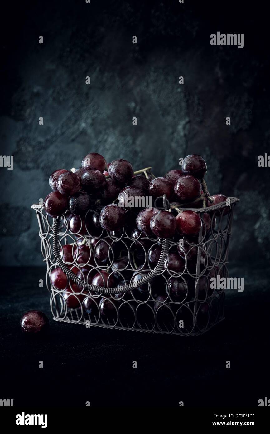 Gros plan d'un bouquet de raisins rouges dans un petit panier à touret, fond noir. Banque D'Images