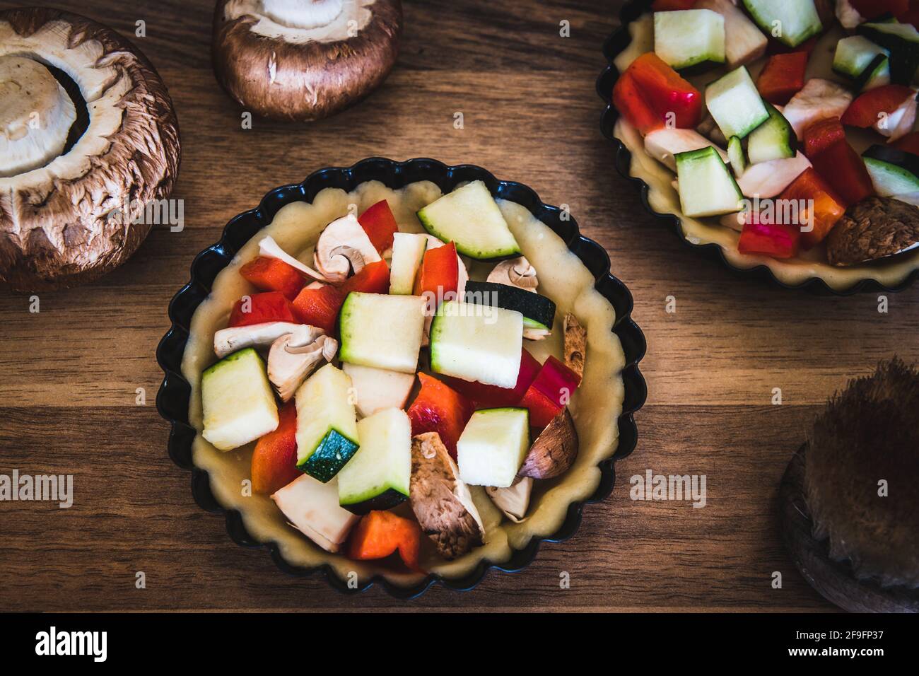 Gros plan de tartelettes de légumes crus dans des plats à tarte noirs sur une table en bois, préparés pour la cuisson. Banque D'Images