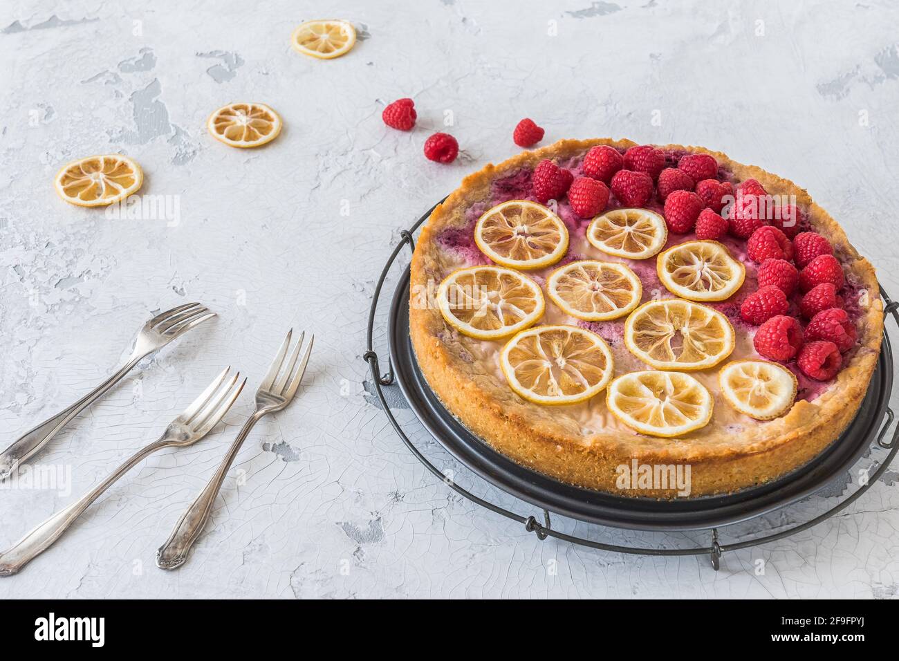 Gâteau au fromage avec framboises et tranches de citron séchées sur fond blanc, quelques framboises, tranches de citron et trois fourchettes sur la table. Banque D'Images