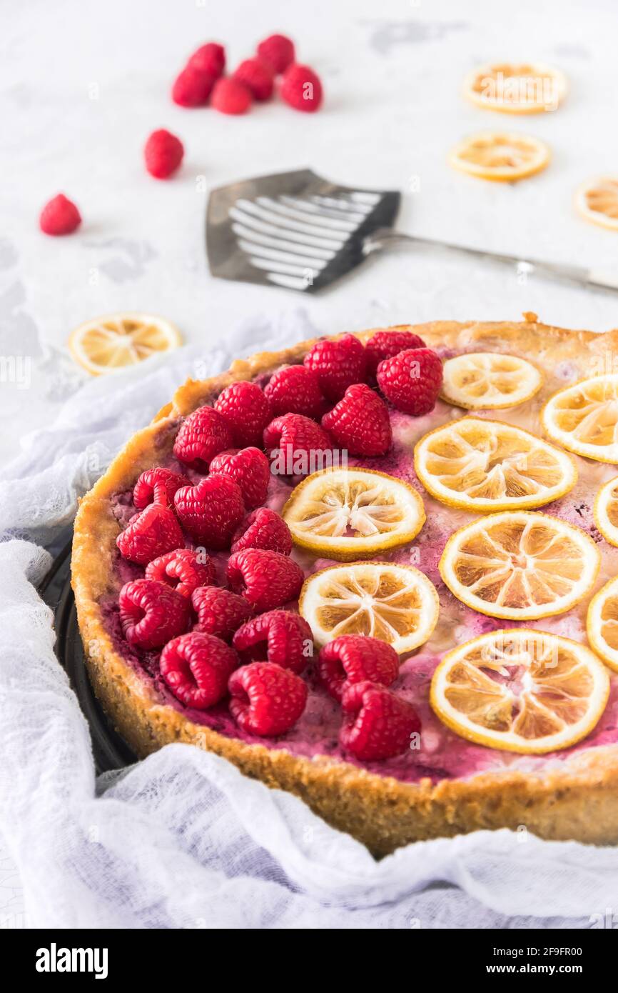 Gâteau au fromage avec framboises et tranches de citron séchées sur fond blanc, quelques framboises, tranches de citron et un serveur à gâteau couché sur la table. C vertical Banque D'Images