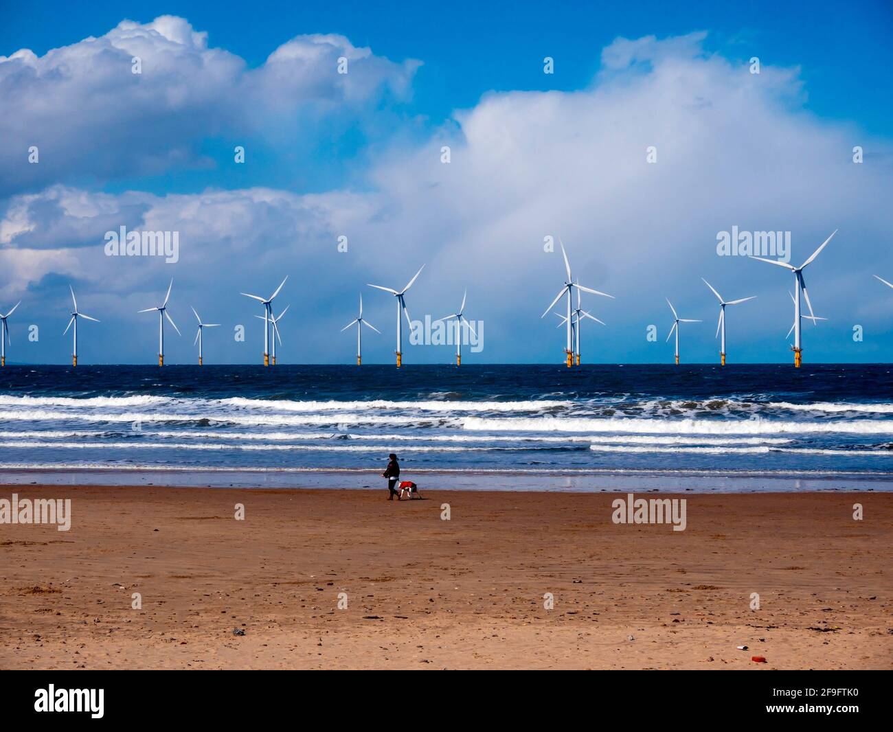 Une femme marchant son chien sur la plage de Coatham au printemps Soleil devant le parc à vent Tees Banque D'Images