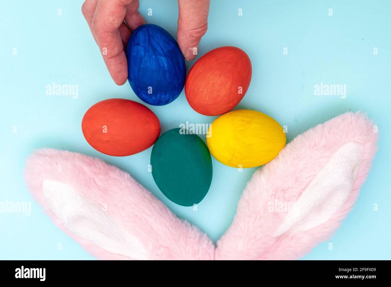 Concept joyeuses Pâques. Pond à la main les œufs de Pâques peints et les oreilles de lapin roses sur fond bleu. Donner des œufs de couleur pour Pâques. Banque D'Images