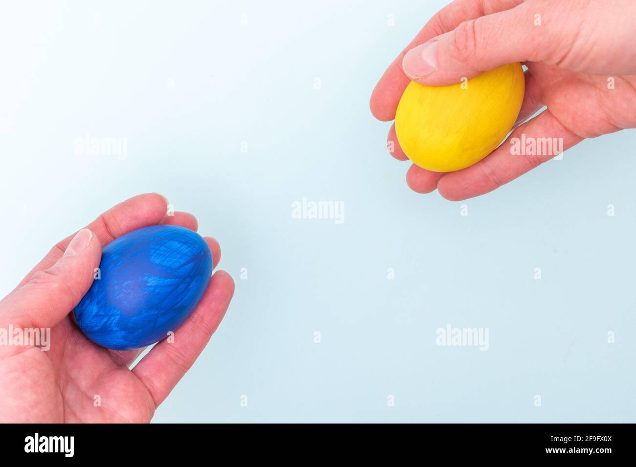 Concept joyeuses Pâques. Deux mains se donnent des œufs de Pâques peints sur fond bleu, gros plan, espace de copie. Les œufs sont un symbole de Pâques. Banque D'Images