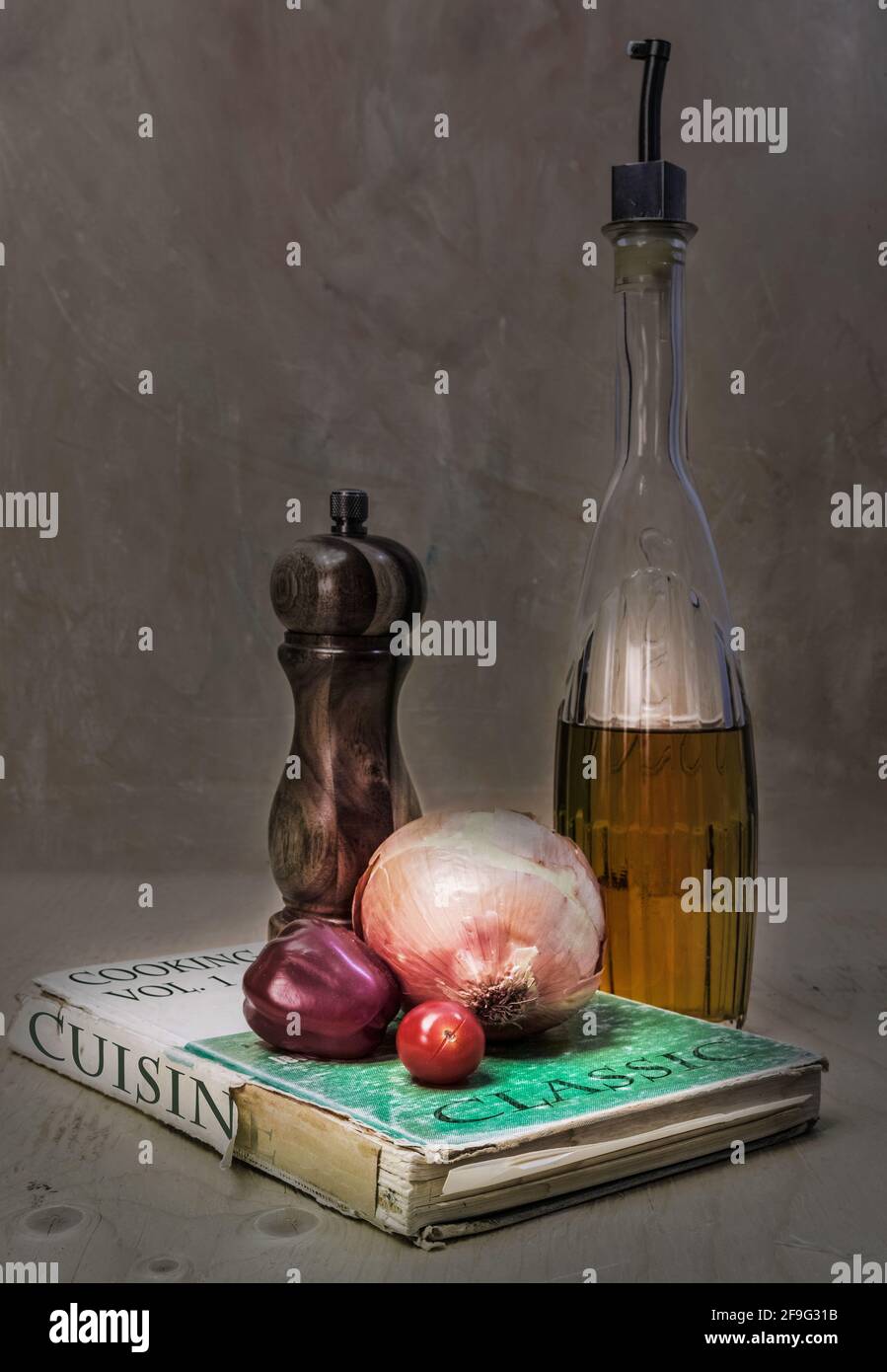 Sur le vieux livre de cuisine légèrement déchiré et surutilisé, nous avons un moulin à poivre, un oignon et une tomate de raisin. À côté, la bouteille d'huile d'olive. Banque D'Images