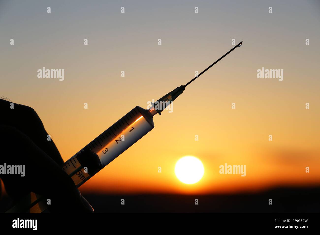 Silhouette de seringue médicale à la main sur fond de coucher de soleil. Concept de vaccination pendant la pandémie de Covid-19 Banque D'Images