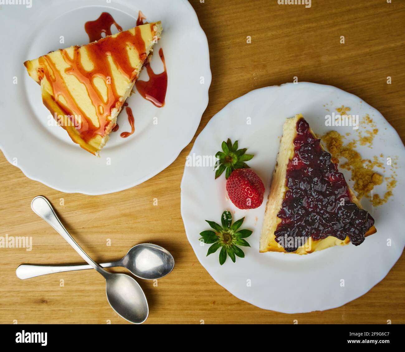 Ensemble de cheesecakes avec une fraise, une sauce aux fraises, des biscuits émiettés et deux cuillères sur fond de bois. Vue de dessus Banque D'Images