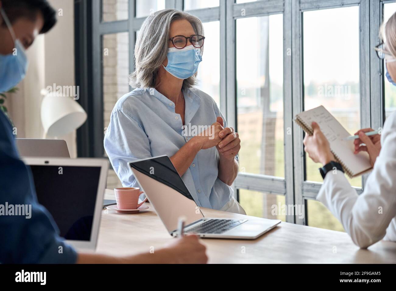 Des personnes travaillant en équipe portant des masques médicaux pendant la réunion au bureau. Banque D'Images