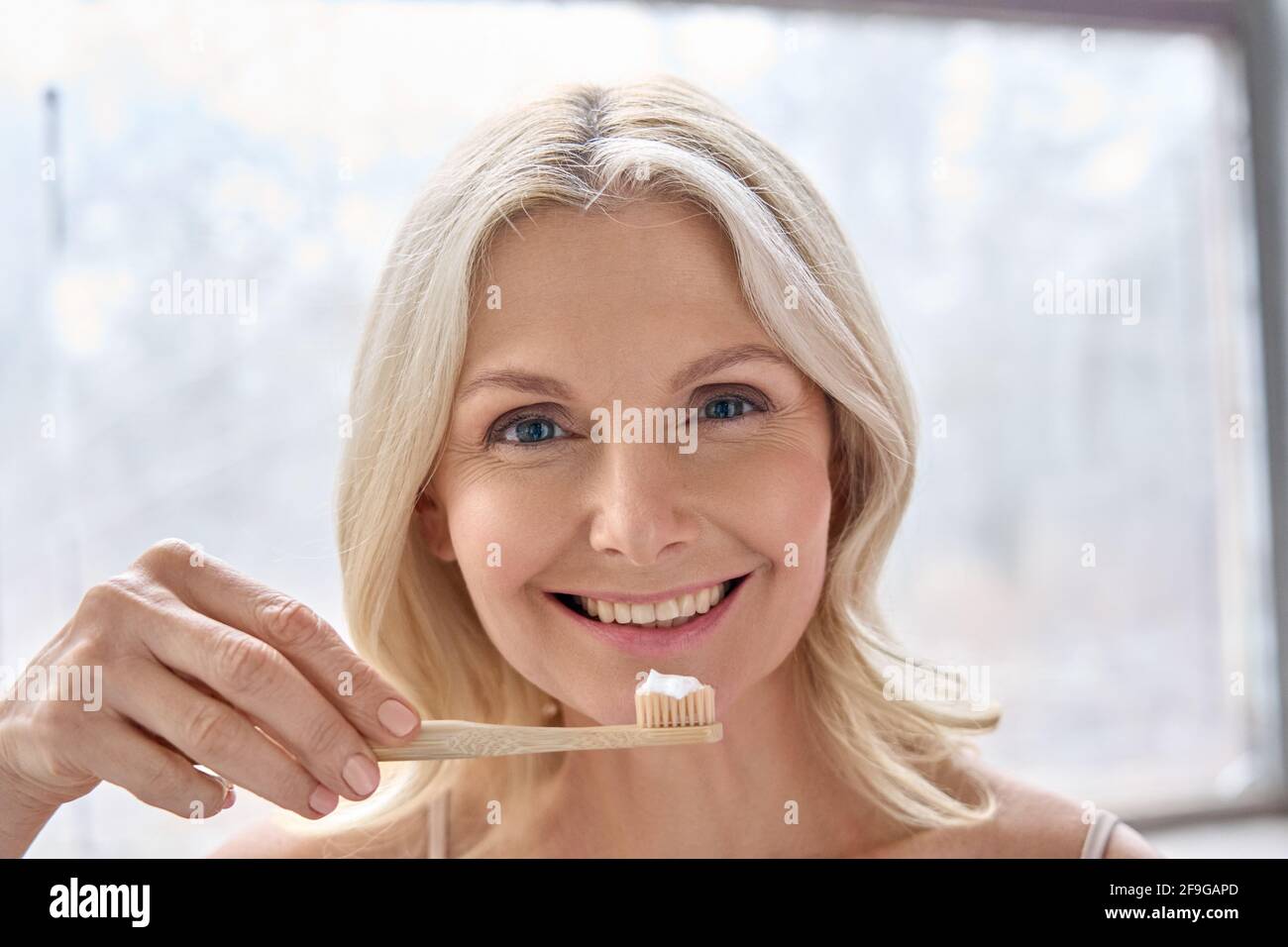 Portrait de femme âgée souriante avec brosse à dents en bambou isolée sur blanc. Banque D'Images