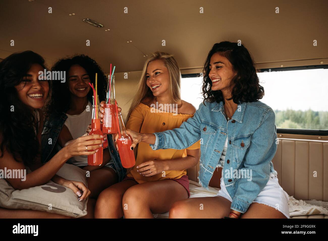Groupe d'amis féminins divers célébrant des vacances. Quatre femmes assises avec des cocktails Banque D'Images