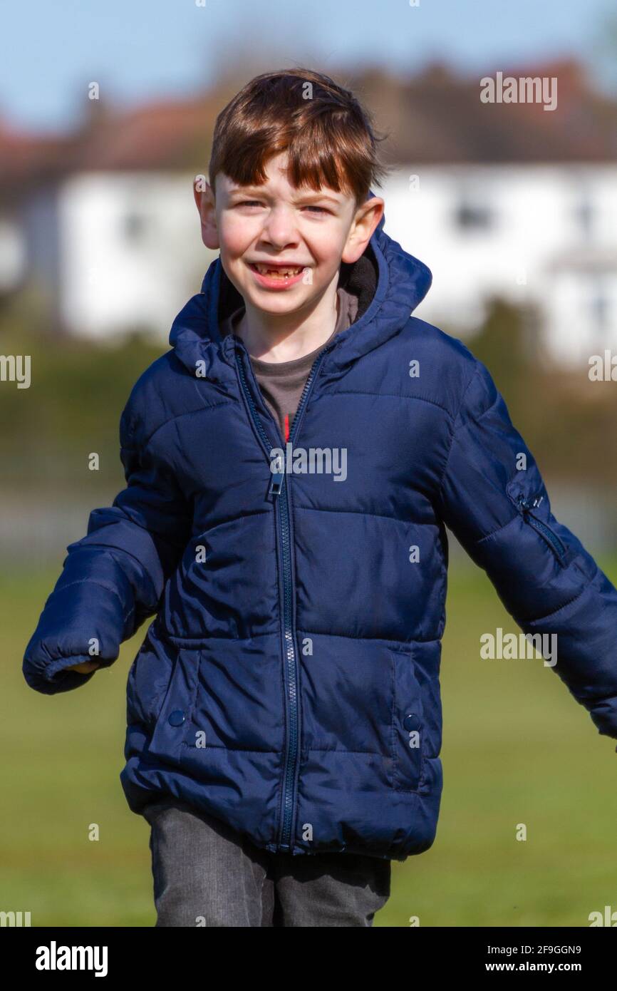 Un adorable garçon à tête rouge aux yeux bleus, portant une veste bleue sur un parc lors d'une journée ensoleillée de printemps Banque D'Images