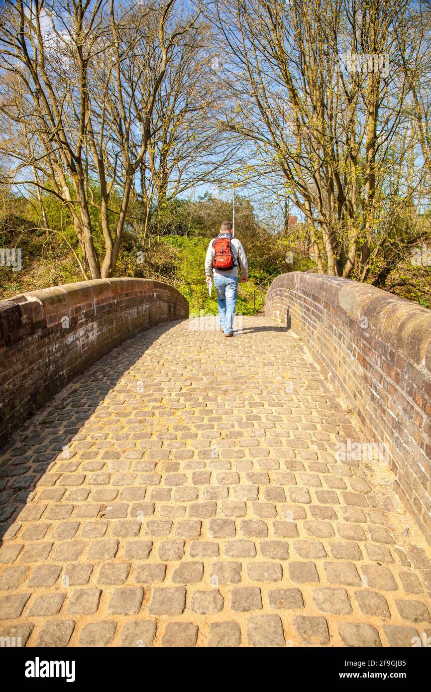 Homme routard qui marche au-dessus d'un vieux pont à cheval avec chariot de canal Au-dessus du canal Trent et Mersey à Kidsgrove Stoke on Trent Staffordshire Banque D'Images