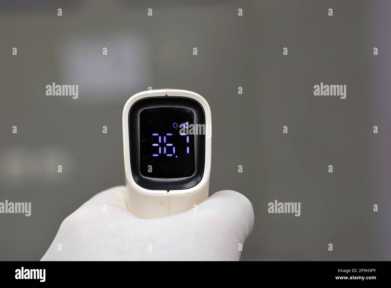 Thermomètre numérique infrarouge frontal sans contact tenu par un jeune homme avec la main gauche et un fond défoqué. Vue en gros plan Banque D'Images